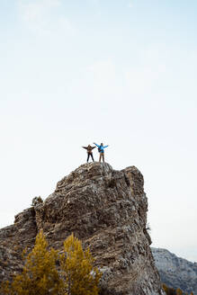 Couple standing on peak of rock mountain against sky - RCPF00405