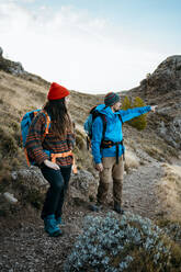 Mittlerer erwachsener Mann, der beim Wandern mit seiner Freundin auf einem felsigen Berg im Urlaub zeigt - RCPF00406