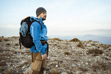 Thoughtful man looking at view while hiking on mountain against sky - RCPF00410