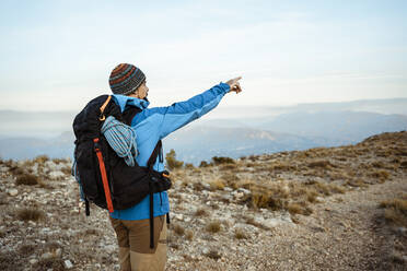 Male hiker pointing while looking at view from mountain during vacation - RCPF00411