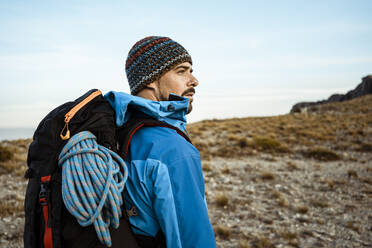 Thoughtful male hiker looking away while standing on mountain against sky - RCPF00412