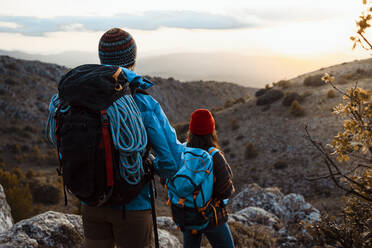 Paar mit Rucksäcken beim Wandern auf einem Berg bei Sonnenuntergang mit Blick auf die Aussicht - RCPF00413