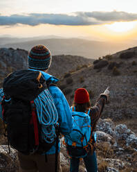 Freundin, die auf einen Berg zeigt, während sie mit ihrem Freund bei Sonnenuntergang wandert - RCPF00414