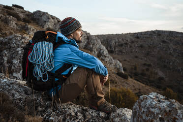 Mittlerer erwachsener Mann, der die Aussicht betrachtet, während er im Urlaub auf einem Felsen am Berg sitzt - RCPF00419