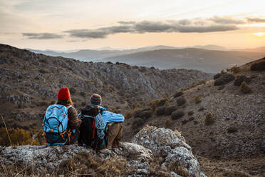 Männliche und weibliche Wanderer genießen den Sonnenuntergang, während sie im Urlaub auf dem Felsenberg sitzen - RCPF00420