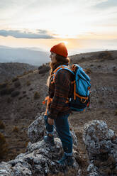 Thoughtful female hiker looking away while standing on rock mountain during sunset - RCPF00422