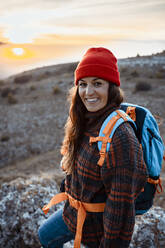 Glückliche Wanderin mit Rucksack auf einem Berg stehend bei Sonnenuntergang - RCPF00423