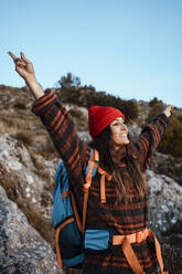 Lächelnde Wanderin mit erhobenen Armen auf felsigem Berg vor klarem Himmel - RCPF00424