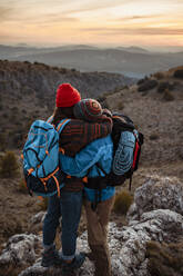 Paar, das sich bei Sonnenuntergang auf einem Berggipfel umarmt - RCPF00435