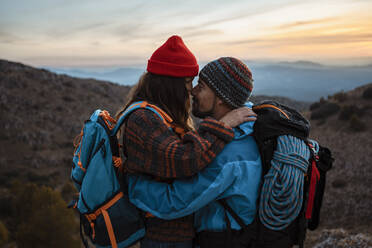 Zärtliches Paar steht von Angesicht zu Angesicht auf einem Berg bei Sonnenuntergang - RCPF00436