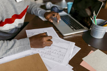 Männlicher Finanzberater, der zu Hause mit dem Laptop eine Strichliste auf Papier erstellt - VABF04080