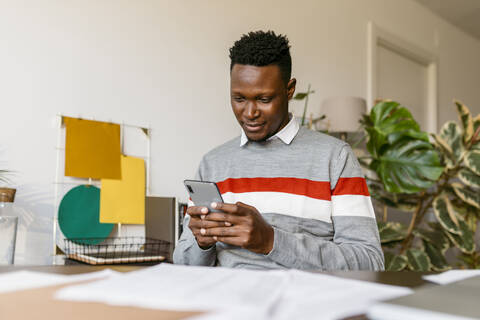 Businessman text messaging on smart phone while working from home stock photo