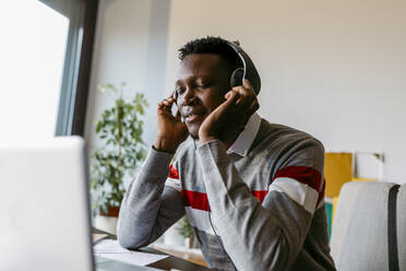 Male freelancer listening music through headphones while taking break from working at home - VABF04089