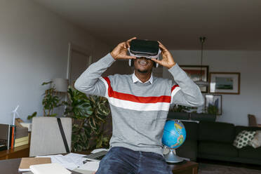 Businessman using virtual reality headset while sitting on desk at home - VABF04095
