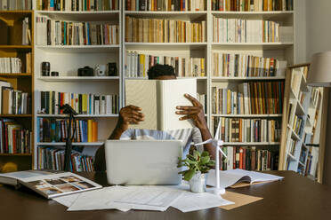 Male environmentalist researching while sitting at desk against bookshelf - VABF04106