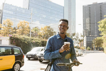 Nachdenklicher männlicher Pendler mit wiederverwendbarem Kaffeebecher, der an einem sonnigen Tag mit einem Elektro-Scooter steht - VABF04122