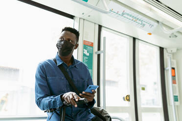 Afrikanischer Geschäftsmann mit Gesichtsschutzmaske während der Fahrt im Zug - VABF04134