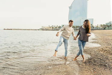 Glückliches junges Paar, das sich bei einem Strandspaziergang gegen den klaren Himmel amüsiert - VABF04142