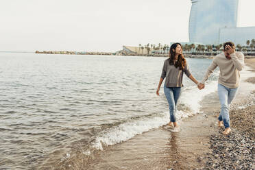 Happy young couple having fun while walking at beach against clear sky - VABF04162