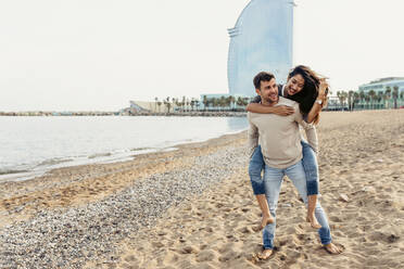 Freund nimmt seine Freundin gegen den Himmel am Strand huckepack - VABF04163
