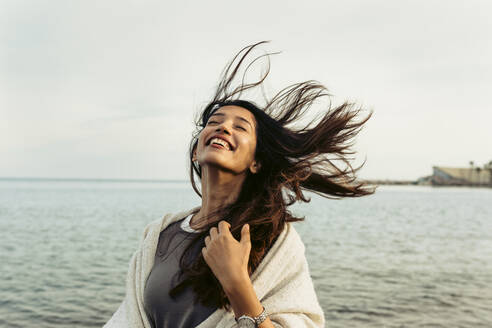 Carefree woman with tousled hair against sky at beach - VABF04181