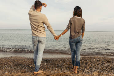 Junges Paar schaut auf das Meer und steht auf Sand - VABF04189