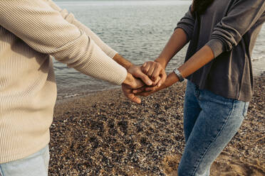 Freundin und Freund stapeln die Hände, während sie am Strand stehen - VABF04194