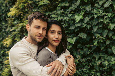 Girlfriend and boyfriend embracing each other against leaves in park - VABF04210