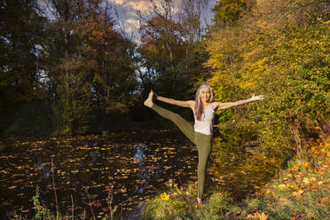 Lächelnde reife Frau übt Yoga gegen Bäume und Teich im Park - FCF01923