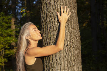 Frau mit geschlossenen Augen umarmt Baum im Park - FCF01929