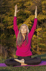 Aktive Frau mit geschlossenen Augen, die die Arme hebt, während sie im Herbst im Park Yoga übt - FCF01934