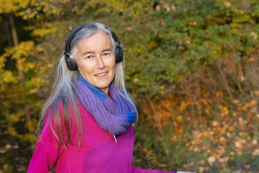 Ältere Frau hört Musik über Kopfhörer im Park - FCF01937