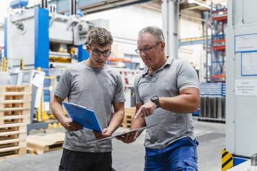 Male coworkers examining product while standing at illuminated factory - DIGF13439