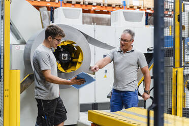 Mature male worker explaining colleague while standing by machinery in industry - DIGF13444