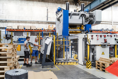 Reife und junge männliche Mitarbeiter testen eine Maschine in einer Fabrik - DIGF13449