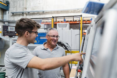 Lächelnde männliche Arbeiter, die eine Maschine in der Industrie untersuchen - DIGF13450