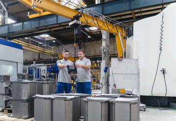 Männliche Angestellte beim Brainstorming, während sie an einer Maschine in einer Fabrik stehen - DIGF13466