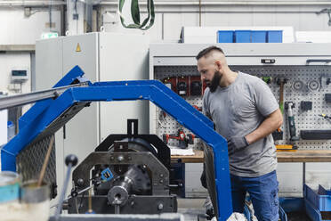 Männlicher Ingenieur betrachtet Maschinen in einer beleuchteten Industriefabrik - DIGF13497