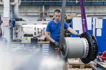 Industrieller männlicher Ingenieur, der eine schwere Maschine in einer beleuchteten Fabrik analysiert - DIGF13504