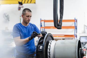 Männlicher Techniker, der eine Maschine repariert, während er in einer beleuchteten Fabrik steht - DIGF13509