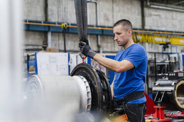 Männlicher Industriearbeiter, der einen Haken an einer Maschine in einer Fabrik anbringt - DIGF13510