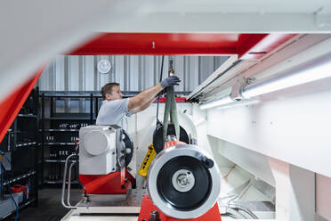 Male technician fastening hook on machine at illuminated modern industry - DIGF13524