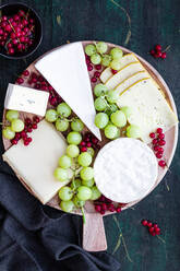 Top view arrangement of delicious cheese plate decorated with sweet grapes and placed on black table near bowl with red currants - ADSF18281