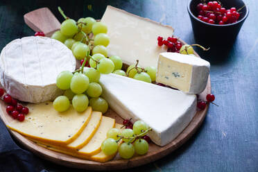 Arrangement of delicious cheese plate decorated with sweet grapes and placed on black table near bowl with red currants - ADSF18284