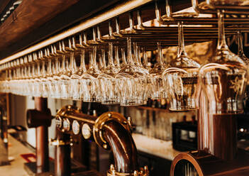 Interieur einer Bar mit glänzenden Gläsern, die auf einem Metallgestell über Bierzapfhähnen in einem Restaurant in Madrid hängen - ADSF18299