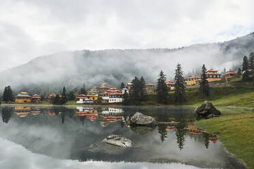 Blick auf alte Gebäude tibetisch-buddhistischer Tempel am Ufer eines ruhigen, spiegelnden Sees im wolkenverhangenen Hochland - ADSF18305
