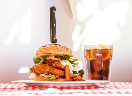 Appetitlicher Hähnchenburger mit Gemüse und Schnitzel auf einem Teller mit Pommes frites, serviert auf dem Tisch mit einem Glas kalter Cola in einem rustikalen Cafe - ADSF18346