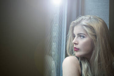 Schöne blonde Frau schaut durch das Fenster - AJOF00703
