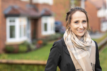 Smiling young woman in scarf standing outside new home - WPEF03705