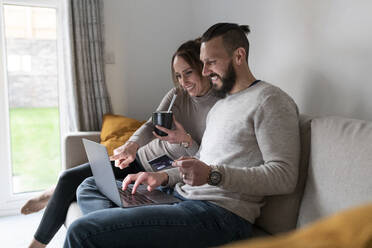 Smiling couple online shopping through laptop while having tea at home - WPEF03719